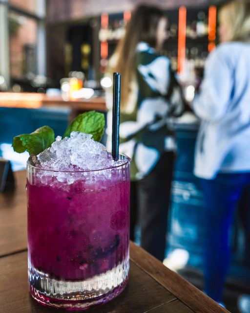 Blueberry Caipiroska made with vodka, frozen blueberry, lime, and agave in a glass with mint garnish and a straw