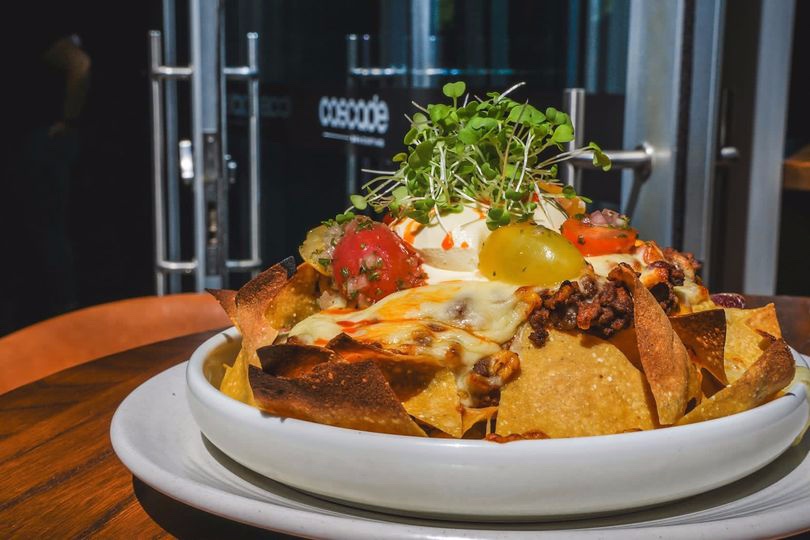 Beef nachos with totopos, tomato salsa, sour cream, and cheese sauce on a plate