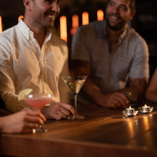 Two men smiling and sitting at the bar with cocktails
